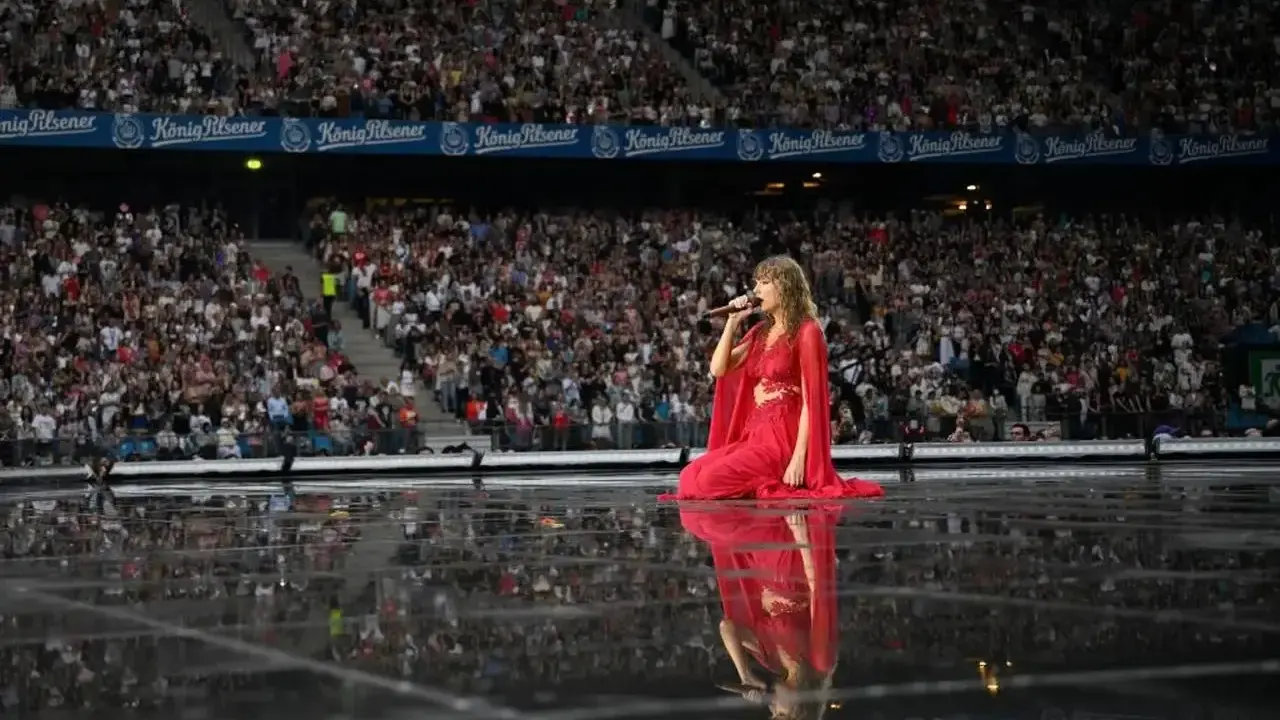 Taylor Swift w czerwonej sukni na scenie, śpiewa dla tłumu. Zastanawiasz się, ile trwa koncert Taylor Swift?