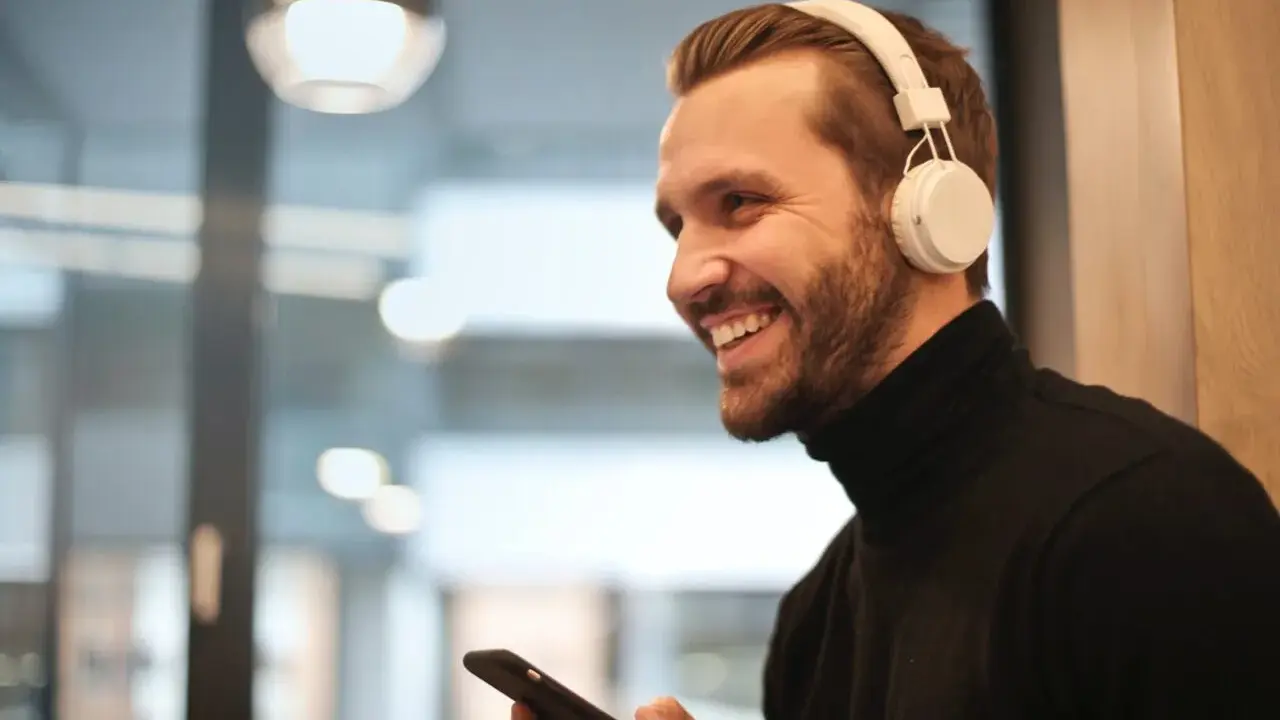 Uśmiechnięty mężczyzna w białych słuchawkach na uszach trzyma telefon, być może właśnie uczy się, jak sparować słuchawki z telefonem.