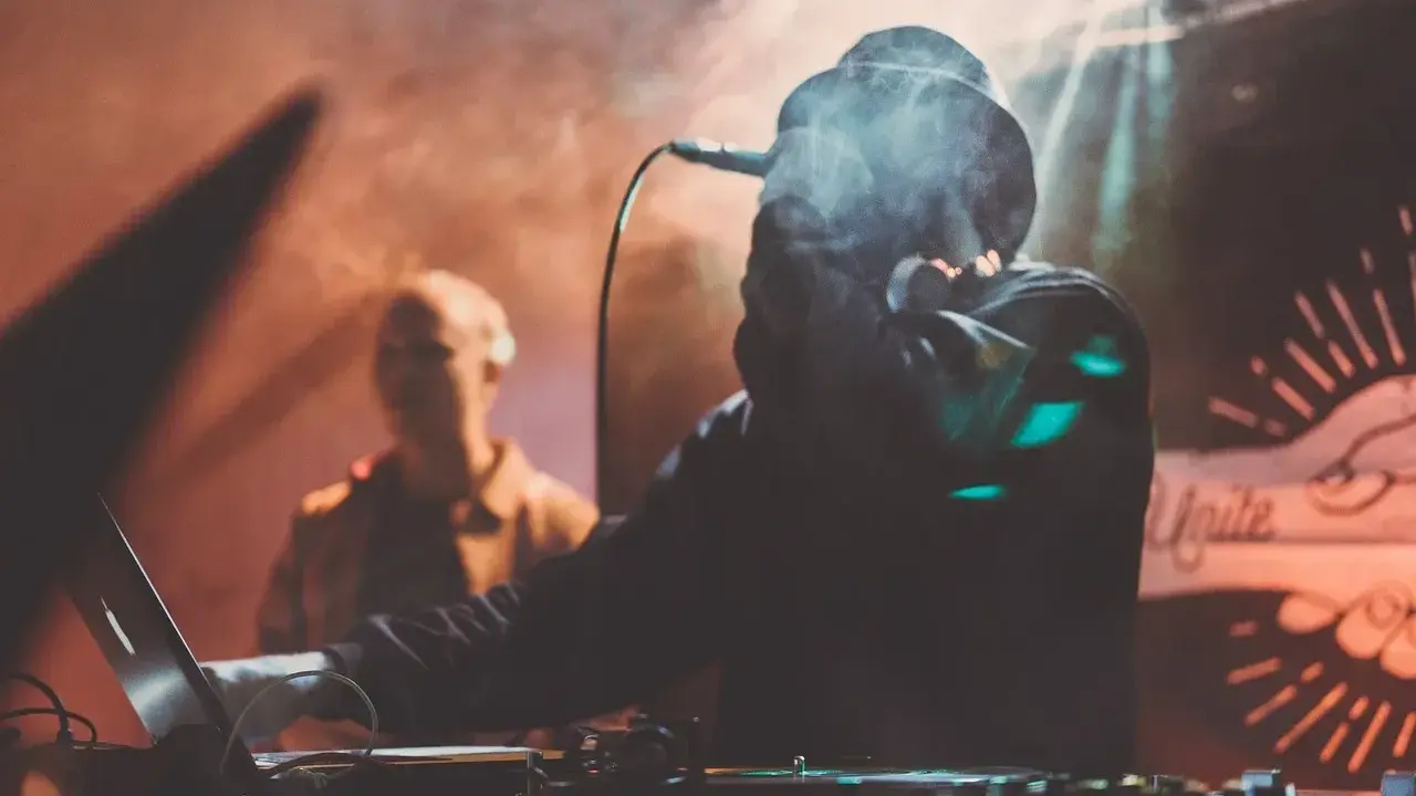 DJ w dymie, z mikrofonem, tworzy muzykę. W tle widać drugą osobę. To jak tekst piosenki "Dni których nie znamy".