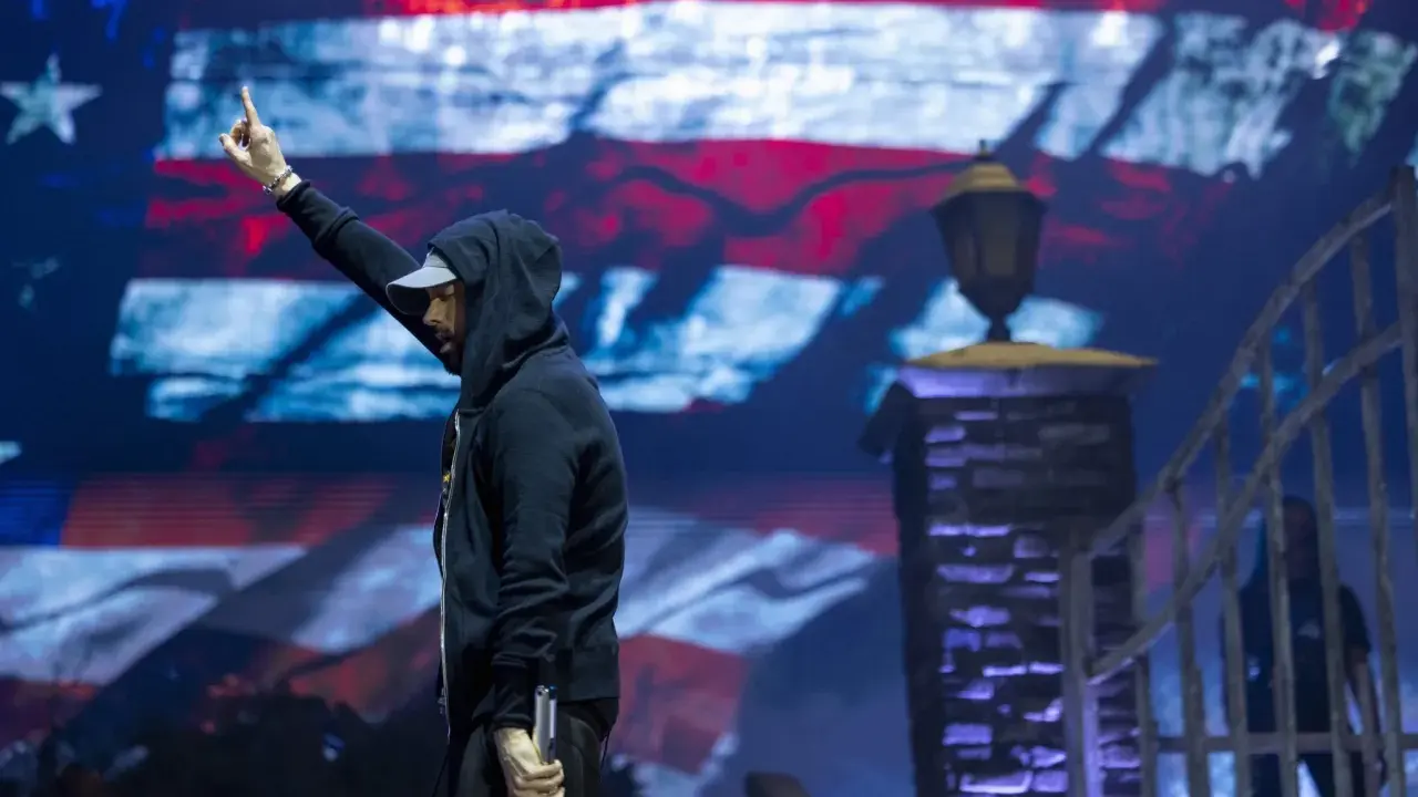Eminem na koncercie, z palcem w górze, na tle amerykańskiej flagi. Czy Eminem nie lubi Polaków? Nie ma dowodów na to w jego twórczości.