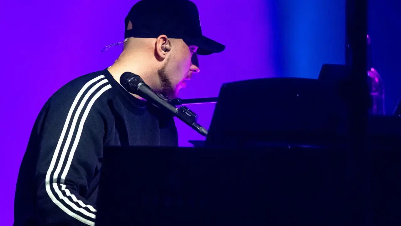 Artysta w czapce z daszkiem gra na pianinie. Koncert Korteza trwa, a fioletowe światło podkreśla atmosferę.