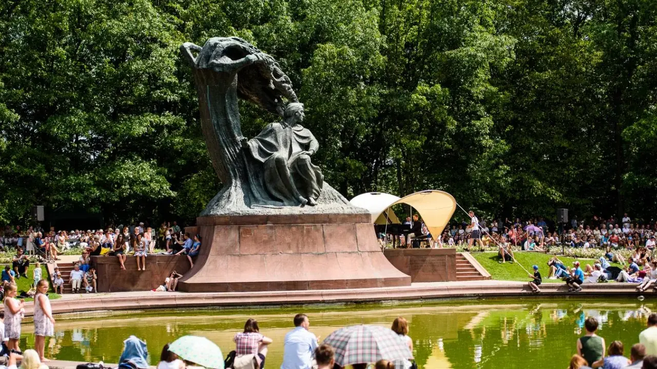 Koncert chopinowski w Łazienkach Królewskich. Tłumy słuchają muzyki przy pomniku Chopina.
