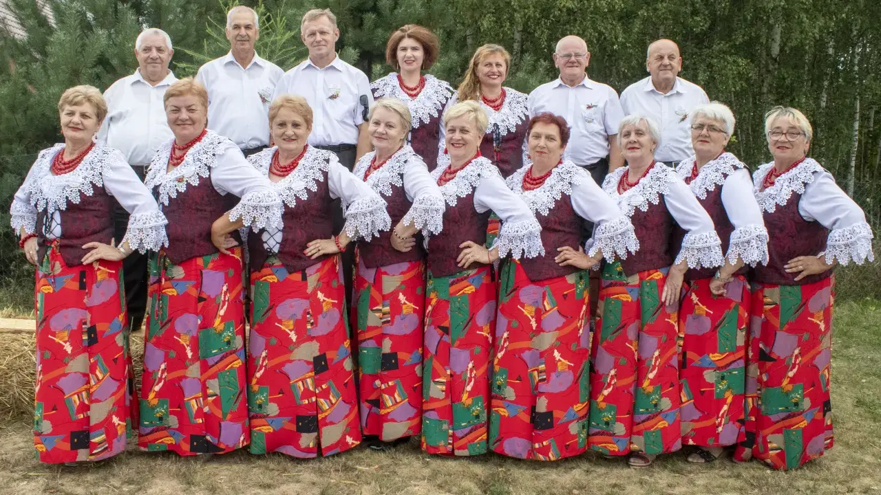 Grupa ludzi w strojach ludowych, kobiety w czerwonych korale i wzorzystych spódnicach, mężczyźni w białych koszulach. Kto śpiewa czerwona jarzębina?