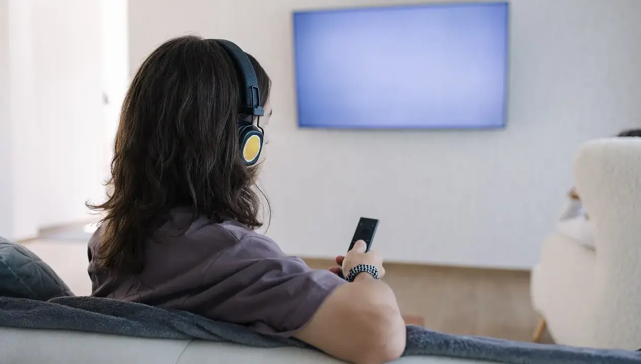 Osoba w słuchawkach z pilotem w ręku, szuka sposobu, jak podłączyć słuchawki bezprzewodowe do telewizora bez bluetooth.
