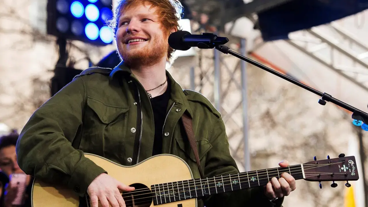 Ed Sheeran uśmiecha się, grając na gitarze akustycznej Martin.