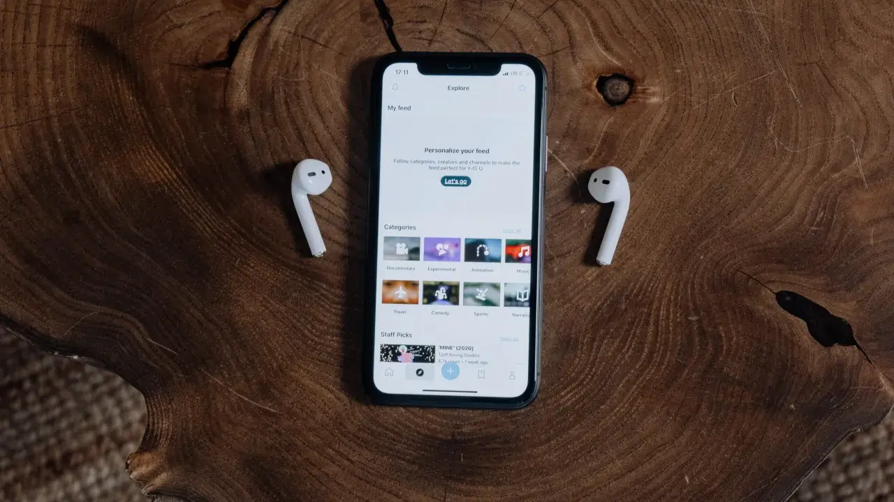 Telefon z aplikacją "Explore" i słuchawki AirPods leżące na drewnianym blacie. Dowiedz się, jak podłączyć AirPods do telefonu.