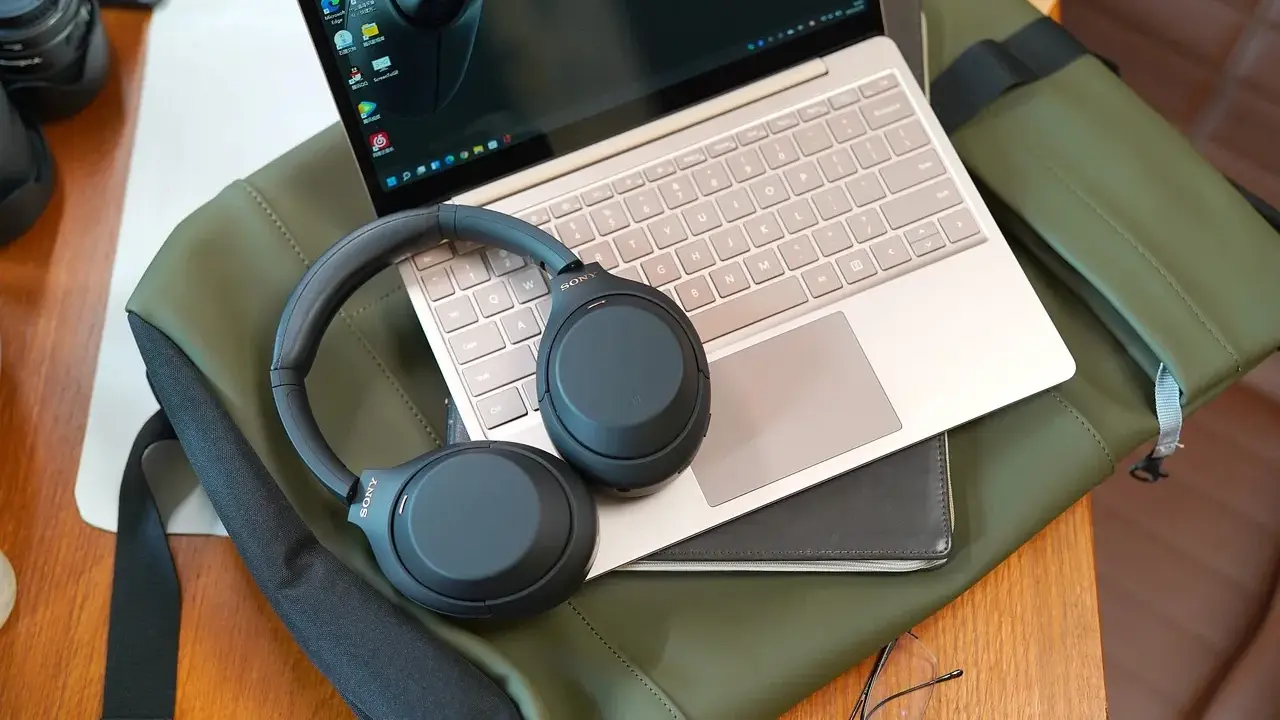 Słuchawki bezprzewodowe Sony leżą na laptopie i zielonej torbie.