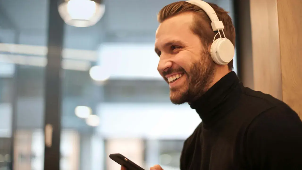 Uśmiechnięty mężczyzna w białych słuchawkach na uszach trzyma smartfon.