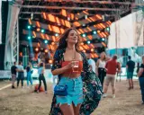 Dziewczyna w kwiecistej narzutce i jeansowej spódniczce, z drinkiem w ręku, pokazuje, jak ubrać się na koncert.