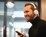 Uśmiechnięty mężczyzna w białych słuchawkach na uszach trzyma telefon, być może właśnie uczy się, jak sparować słuchawki z telefonem.
