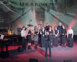 Grupa artystów na scenie, gdzie odbywa się koncert dla Ukrainy. W tle ekran z napisem "UKRAINE".