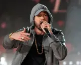 Eminem w szarej bluzie z kapturem i złotym łańcuchem śpiewa do mikrofonu.