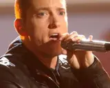 Eminem śpiewa do mikrofonu. Choć jego wzrost, czyli ile Eminem ma wzrostu, nie jest widoczny, jego energia na scenie jest ogromna.