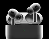 Białe słuchawki AirPods Pro w etui z zieloną diodą, na czarnym tle.