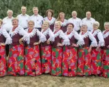 Grupa ludzi w strojach ludowych, kobiety w czerwonych korale i wzorzystych spódnicach, mężczyźni w białych koszulach. Kto śpiewa czerwona jarzębina?