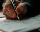 Dłoń pisze długopisem na kartce, tworząc tekst. To inspiracja, jak pisać teksty piosenek, rodzące się z myśli.