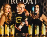 Trzy osoby pozują z butelką wódki Ruda. W tle widać drinki i logo.