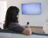 Osoba w słuchawkach z pilotem w ręku, szuka sposobu, jak podłączyć słuchawki bezprzewodowe do telewizora bez bluetooth.
