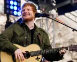 Ed Sheeran uśmiecha się, grając na gitarze akustycznej Martin.