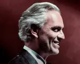 Uśmiechnięty Andrea Bocelli w garniturze, z siwymi włosami, w profilu. To zapowiedź, gdzie koncert Bocellego.