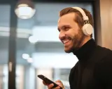 Uśmiechnięty mężczyzna w słuchawkach na uszach trzyma telefon. Proste jak podłączyć słuchawki przewodowe do telefonu Samsung.