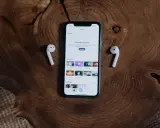 Telefon z aplikacją "Explore" i słuchawki AirPods leżące na drewnianym blacie. Dowiedz się, jak podłączyć AirPods do telefonu.