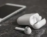 Białe słuchawki bezprzewodowe i smartfon na ciemnym tle. Jedna słuchawka leży obok etui, zastanawiasz się, dlaczego działa tylko jedna słuchawka bezprzewodowa?