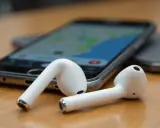 Białe słuchawki AirPods leżą obok telefonu z mapą. Zastanawiasz się, jak znaleźć airpods w domu? Użyj funkcji "Znajdź mój iPhone".