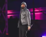 Eminem na scenie w szarej bluzie z kapturem i czarnych spodniach, trzymający mikrofon.