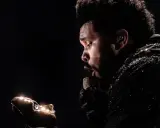 The Weeknd w błyszczącej kurtce, z mikrofonem w dłoni, zastanawia się, ile trwa koncert The Weeknd.
