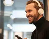 Uśmiechnięty mężczyzna w białych słuchawkach na uszach trzyma smartfon.
