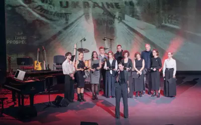 Grupa artystów na scenie, gdzie odbywa się koncert dla Ukrainy. W tle ekran z napisem "UKRAINE".