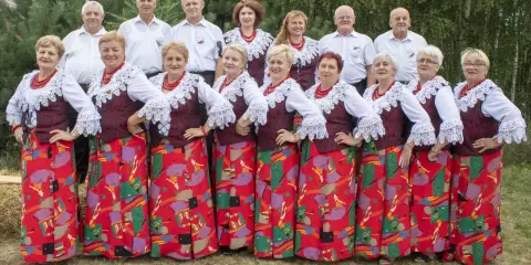 Grupa ludzi w strojach ludowych, kobiety w czerwonych korale i wzorzystych spódnicach, mężczyźni w białych koszulach. Kto śpiewa czerwona jarzębina?