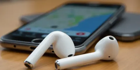 Białe słuchawki AirPods leżą obok telefonu z mapą. Zastanawiasz się, jak znaleźć airpods w domu? Użyj funkcji "Znajdź mój iPhone".