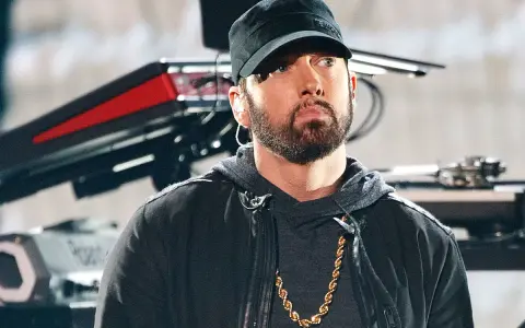Eminem w czapce i z łańcuchem na szyi. W tle sprzęt muzyczny. Ciekawe, ile ma lat Eminem?