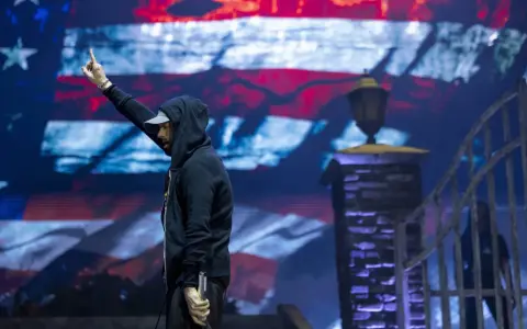 Eminem na koncercie, z palcem w górze, na tle amerykańskiej flagi. Czy Eminem nie lubi Polaków? Nie ma dowodów na to w jego twórczości.