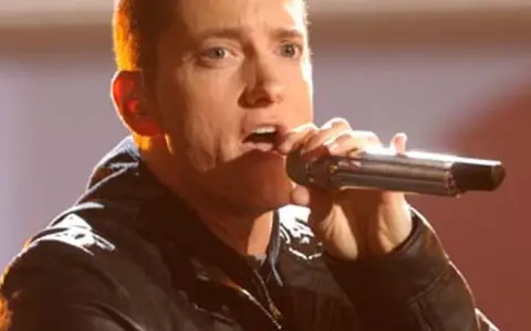 Eminem śpiewa do mikrofonu. Choć jego wzrost, czyli ile Eminem ma wzrostu, nie jest widoczny, jego energia na scenie jest ogromna.
