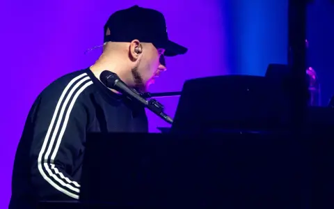 Artysta w czapce z daszkiem gra na pianinie. Koncert Korteza trwa, a fioletowe światło podkreśla atmosferę.