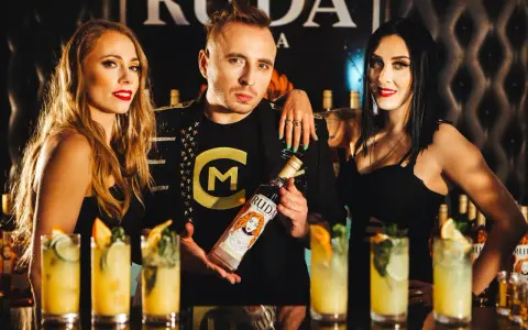Trzy osoby pozują z butelką wódki Ruda. W tle widać drinki i logo.