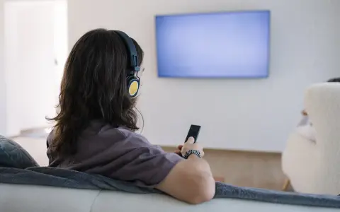 Osoba w słuchawkach z pilotem w ręku, szuka sposobu, jak podłączyć słuchawki bezprzewodowe do telewizora bez bluetooth.
