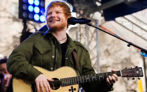 Ed Sheeran uśmiecha się, grając na gitarze akustycznej Martin.