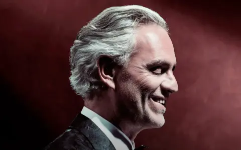 Uśmiechnięty Andrea Bocelli w garniturze, z siwymi włosami, w profilu. To zapowiedź, gdzie koncert Bocellego.