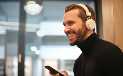 Uśmiechnięty mężczyzna w słuchawkach na uszach trzyma telefon. Proste jak podłączyć słuchawki przewodowe do telefonu Samsung.