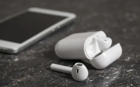Białe słuchawki bezprzewodowe i smartfon na ciemnym tle. Jedna słuchawka leży obok etui, zastanawiasz się, dlaczego działa tylko jedna słuchawka bezprzewodowa?
