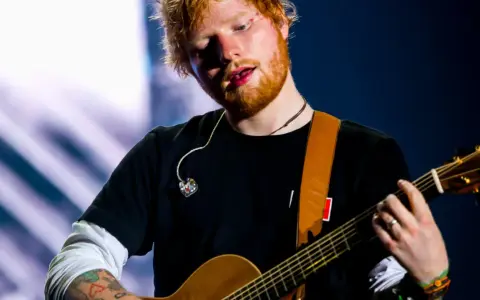 Ed Sheeran gra na gitarze, a jego wiek to 33 lata.