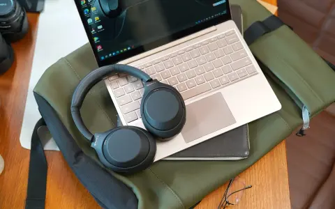 Słuchawki bezprzewodowe Sony leżą na laptopie i zielonej torbie.