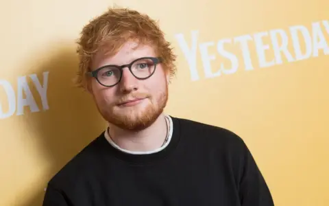Ed Sheeran w okularach i czarnej bluzie, na tle napisu "YESTERDAY". Wygląda jakby zastanawiał się, kiedy urodził się Ed Sheeran.
