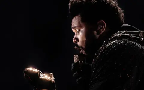The Weeknd w błyszczącej kurtce, z mikrofonem w dłoni, zastanawia się, ile trwa koncert The Weeknd.