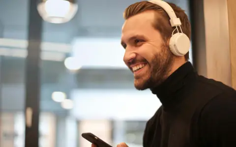 Uśmiechnięty mężczyzna w białych słuchawkach na uszach trzyma smartfon.