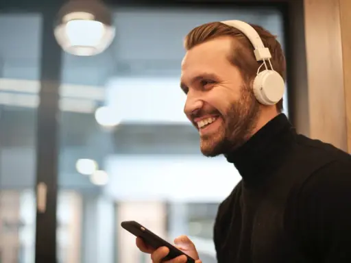 Uśmiechnięty mężczyzna w białych słuchawkach na uszach trzyma telefon, być może właśnie uczy się, jak sparować słuchawki z telefonem.